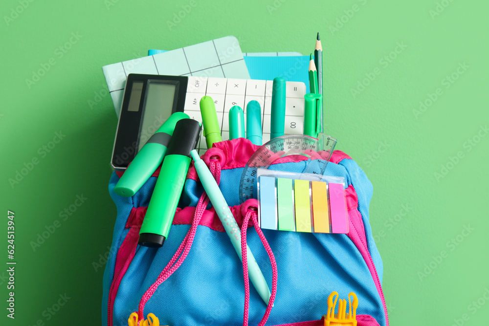 School backpack with different stationery on green background