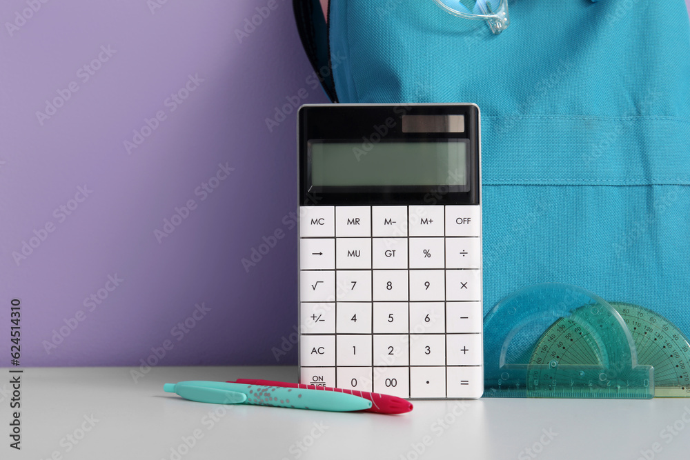 Blue school backpack with stationery and calculator on white table near purple wall