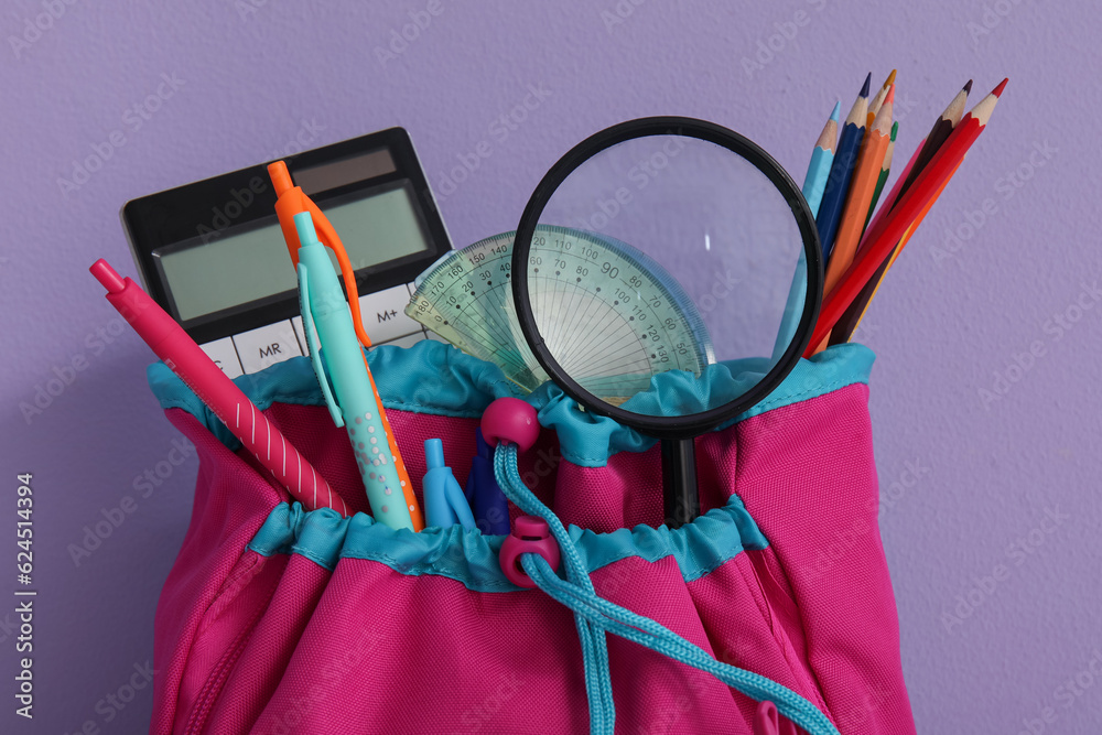 Colorful school backpack with different stationery and magnifier on purple background