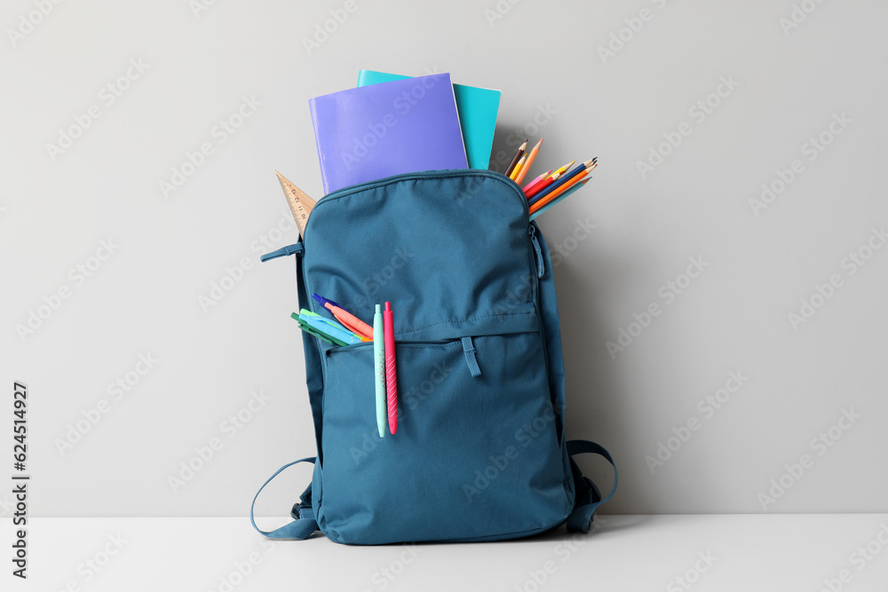 Blue school backpack with different stationery on white table near wall