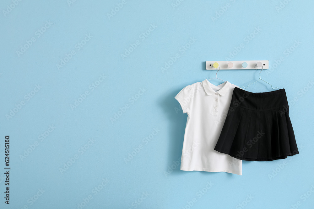 Stylish school uniform hanging on blue wall in room