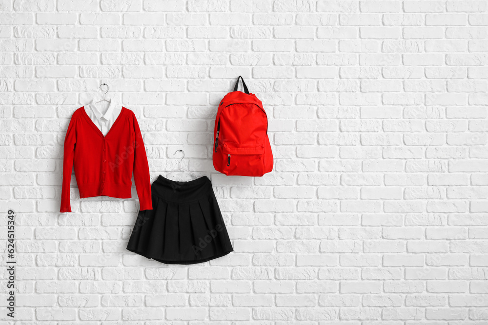 Stylish school uniform and backpack hanging on light brick wall in room