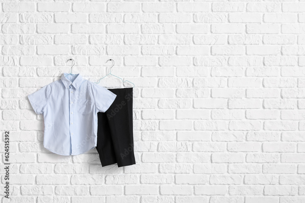 Stylish school uniform hanging on light brick wall in room