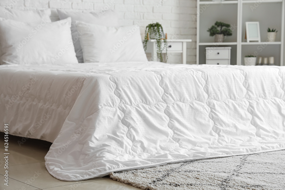 Cozy bed with white blanket and pillows in interior of light bedroom