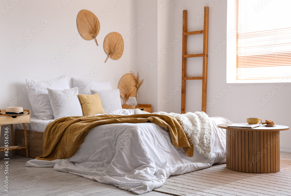 Cozy bed with white blanket and coffee table in interior of light bedroom