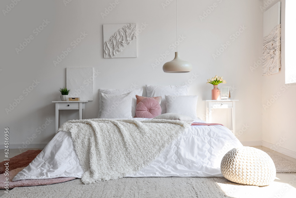 Cozy bed with white blanket and pillows in interior of light bedroom