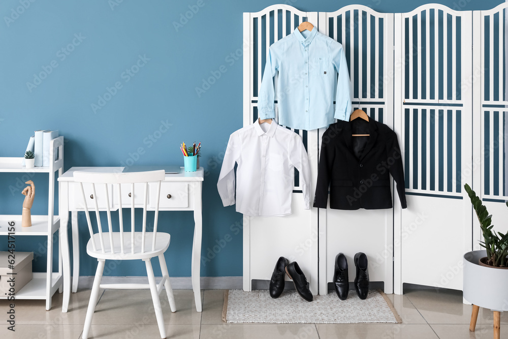 Stylish school uniform hanging on folding screen and shoes in room