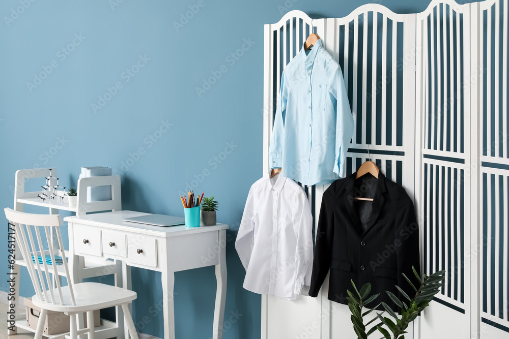 Stylish school uniform hanging on folding screen in childrens room