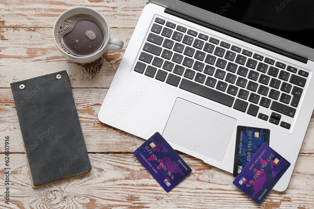 Laptop with credit cards, notebook and cup of coffee on light wooden background