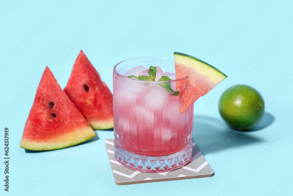 Glass of tasty watermelon cocktail with mint and lime on blue background