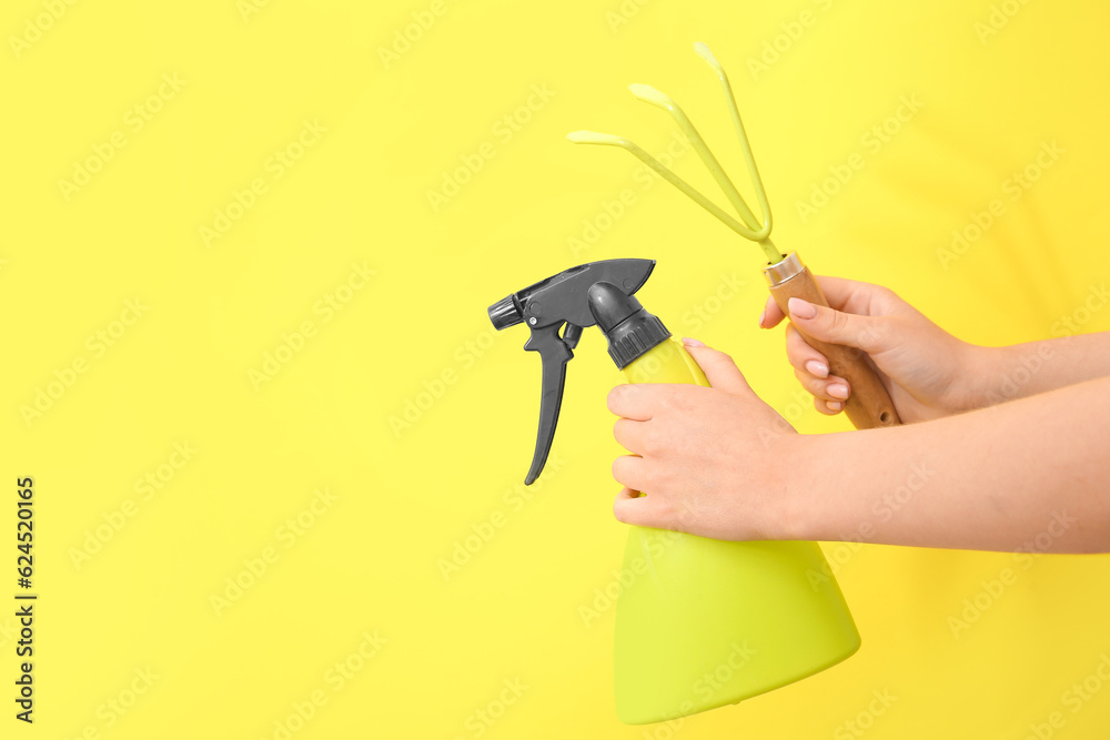 Woman with gardening rake and water spray on yellow background