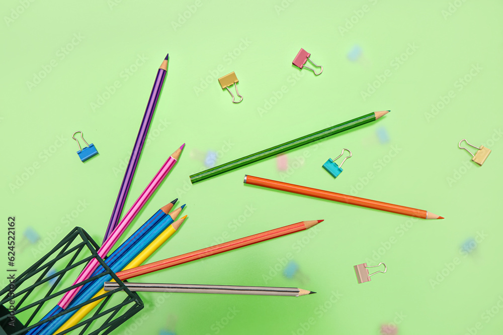 Overturned pen cup with colorful pencils and paperclips on green background