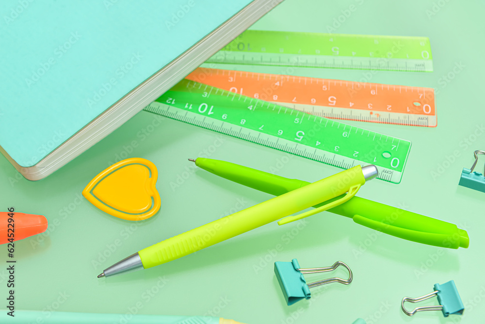 Pens, rulers and paperclips on green background