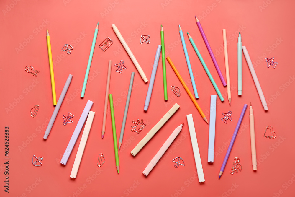 Colorful pencils and markers with paper clips in different shapes on red background