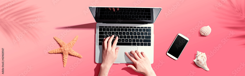 Person using a laptop computer with shells and starfish - flat lay