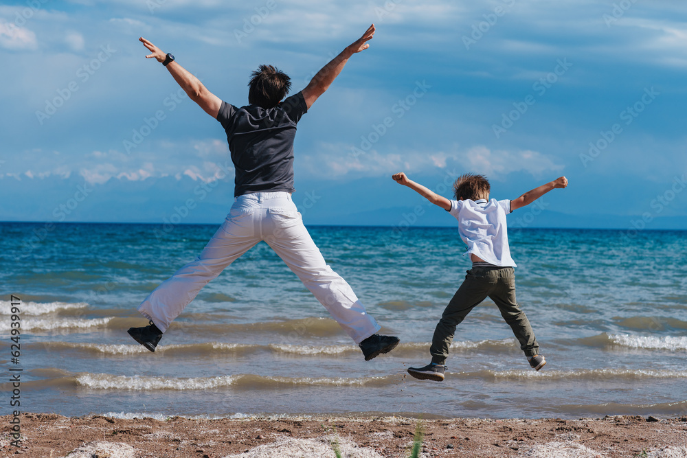 Happy father and son jumping on shore of the lake