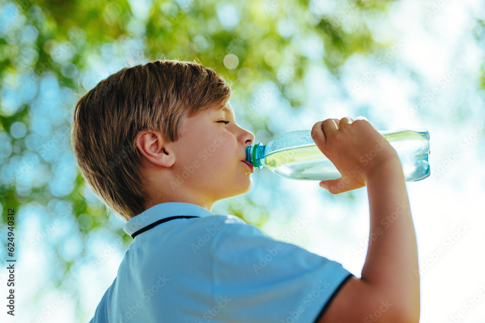 Portrait of boy drinking pure water from a bottle on a sunny day in nature