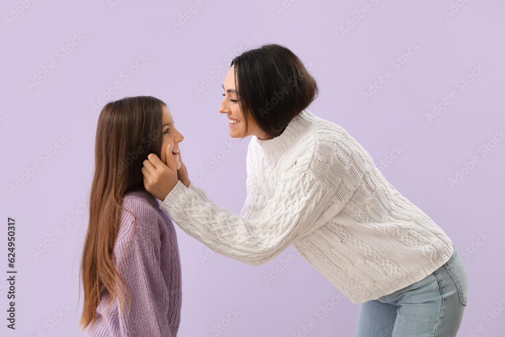 Little girl and her mother in warm sweaters on lilac background