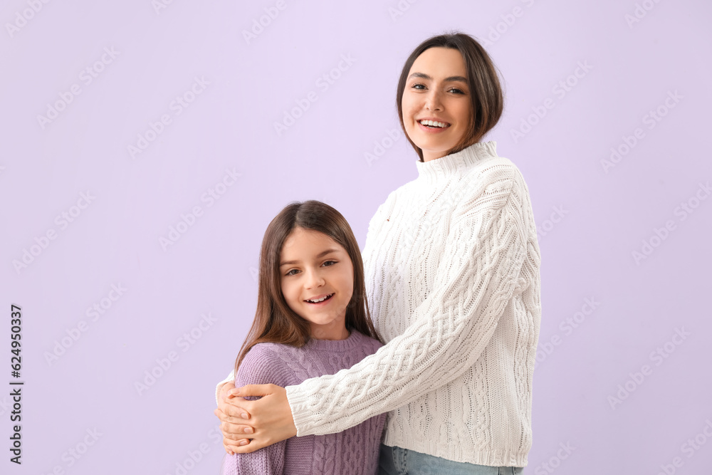 Little girl and her mother in warm sweaters on lilac background