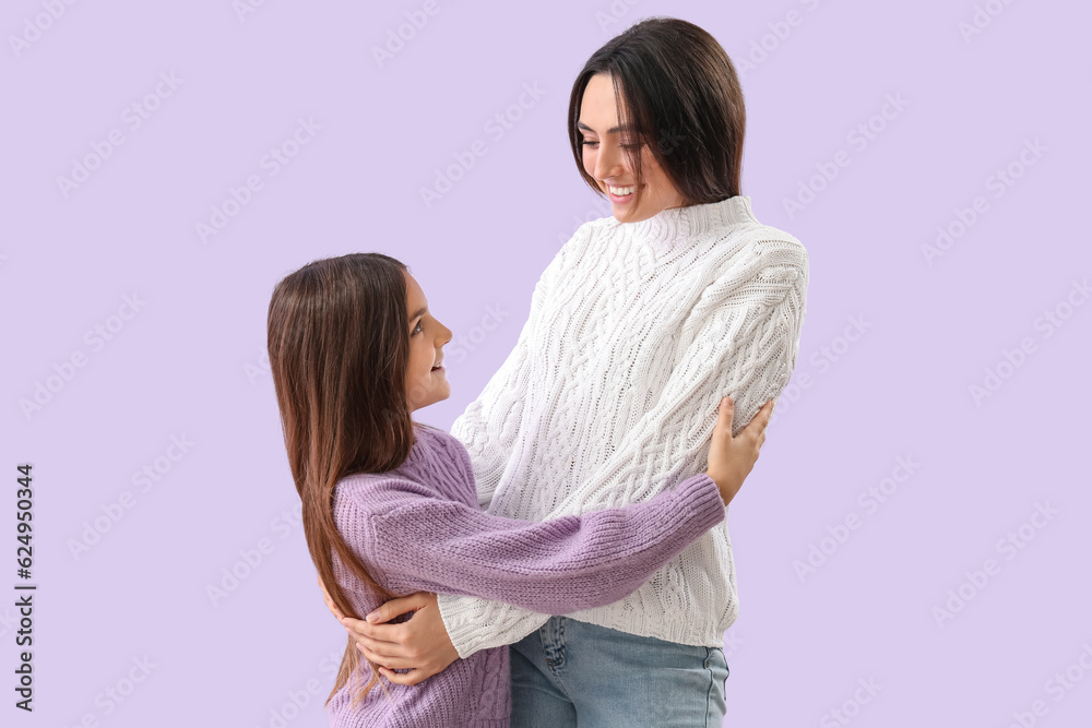 Little girl and her mother in warm sweaters hugging on lilac background