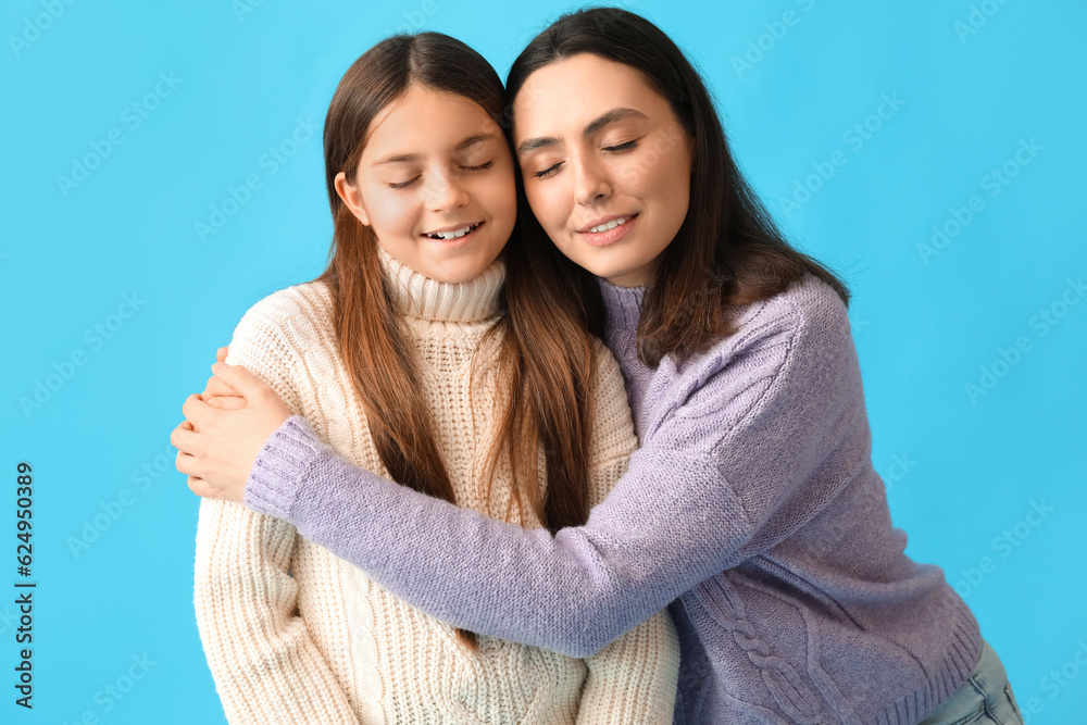 Little girl and her mother in knitted sweaters hugging on blue background