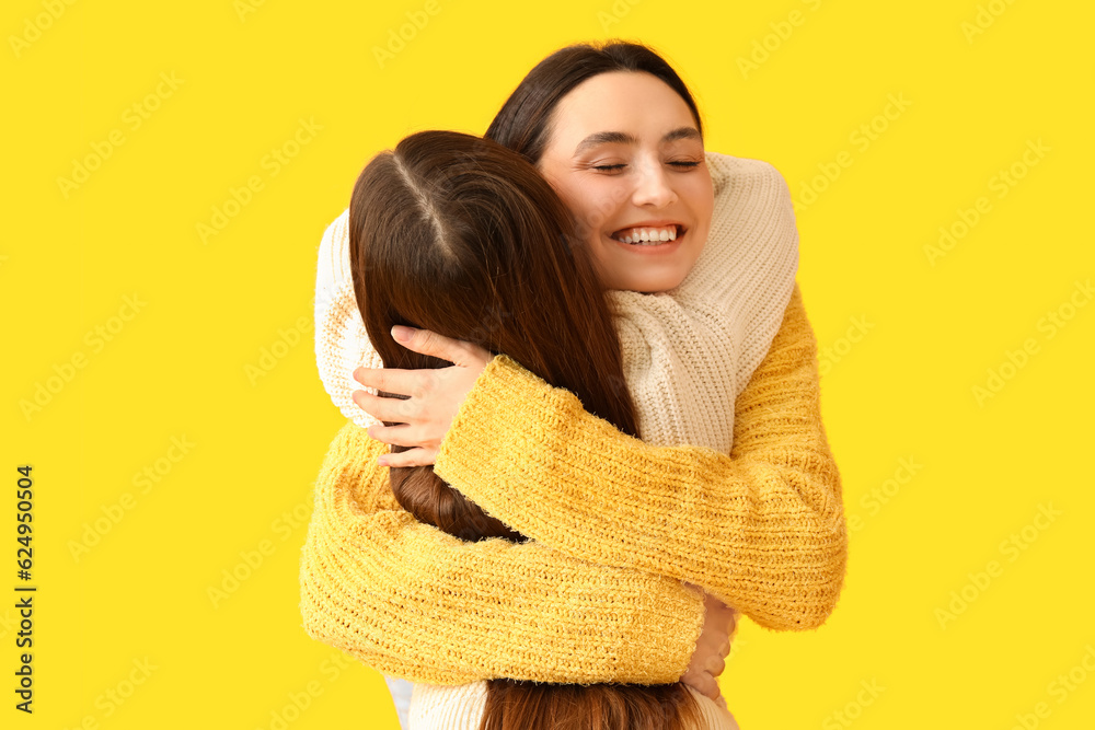 Little girl and her mother in knitted sweaters hugging on yellow background