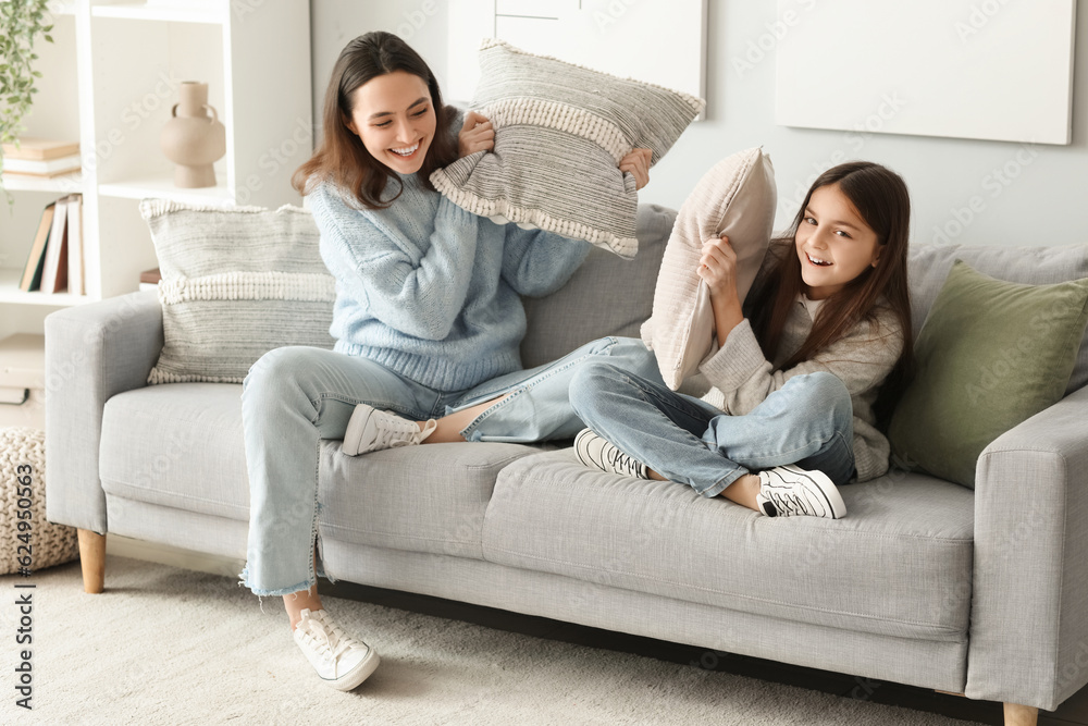 Little girl and her mother in warm sweaters fighting pillows at home