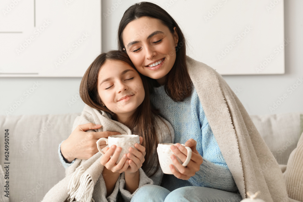 Little girl and her mother with cups of tea sitting at home