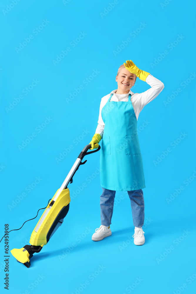 Tired young woman with vacuum cleaner on blue background