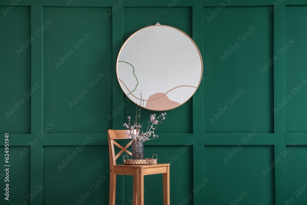 Vase with blooming branches on stool near mirror in room