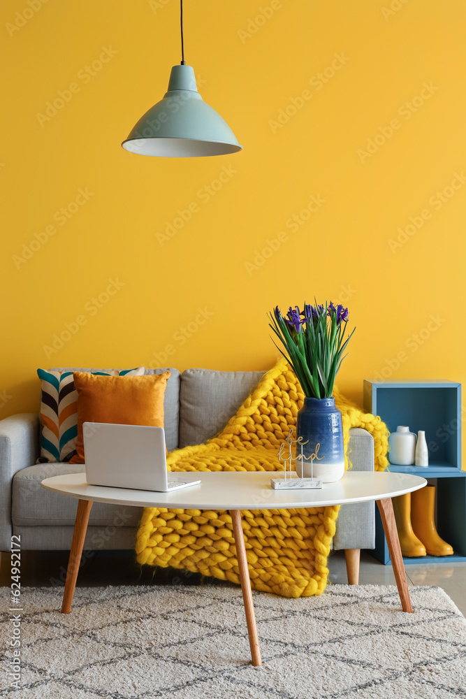 Interior of stylish living room with grey sofa, iris flowers and modern laptop on coffee table