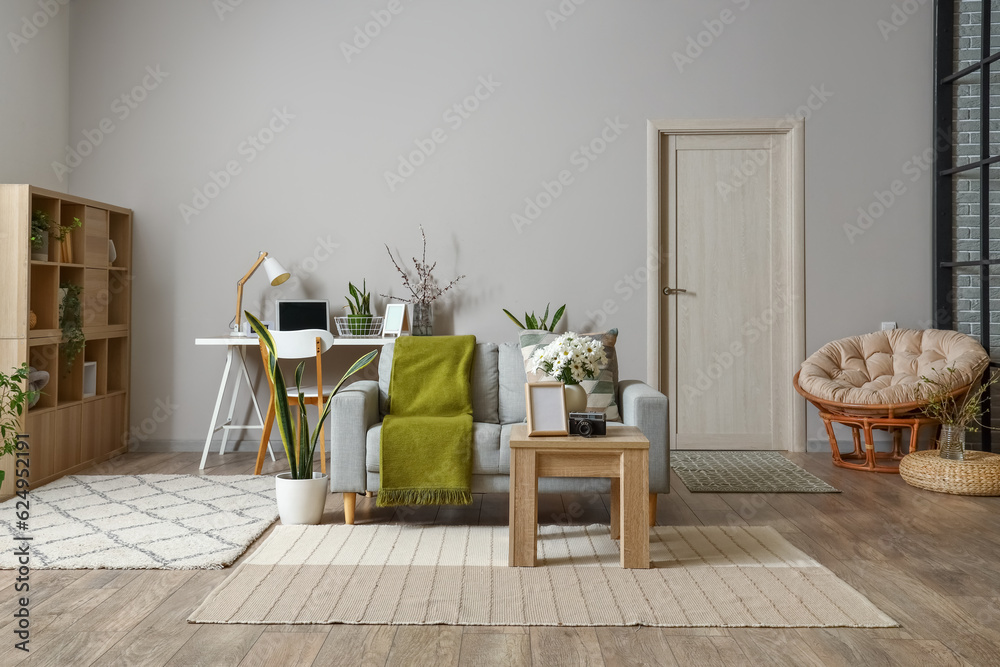 Interior of modern living room with grey sofa, workplace and blooming chrysanthemum flowers on table