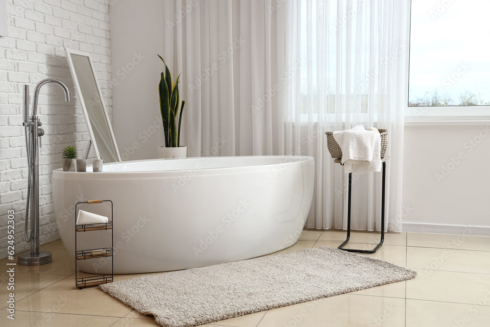 Interior of light bathroom with big bathtub near window