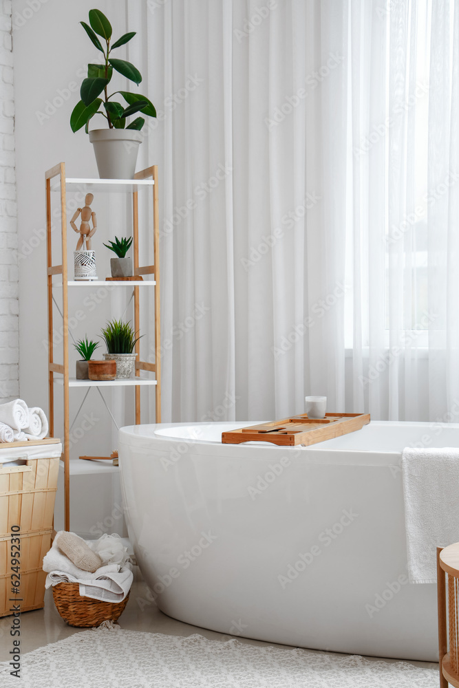 Interior of light bathroom with bathtub and shelving unit