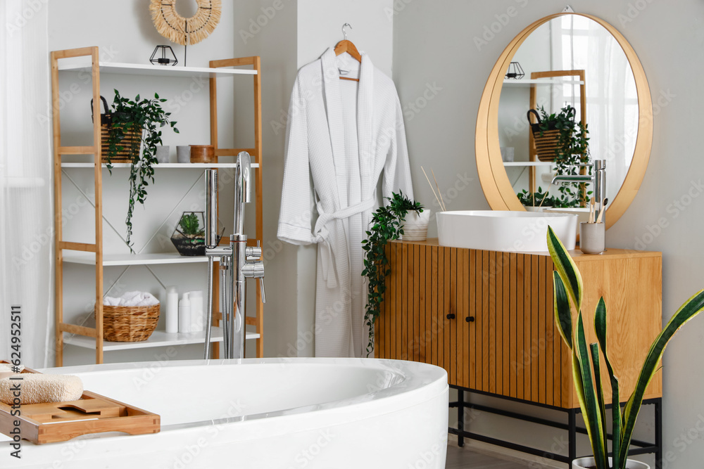 Interior of light bathroom with bathtub, wooden cabinet and mirror