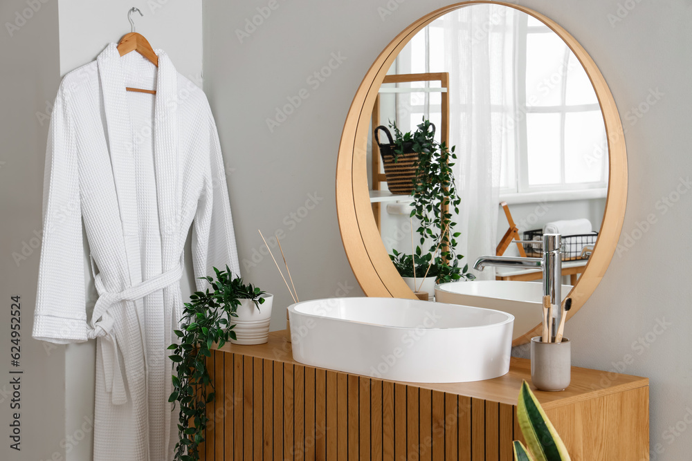 Wooden cabinet with sink bowl, faucet and mirror in interior of bathroom