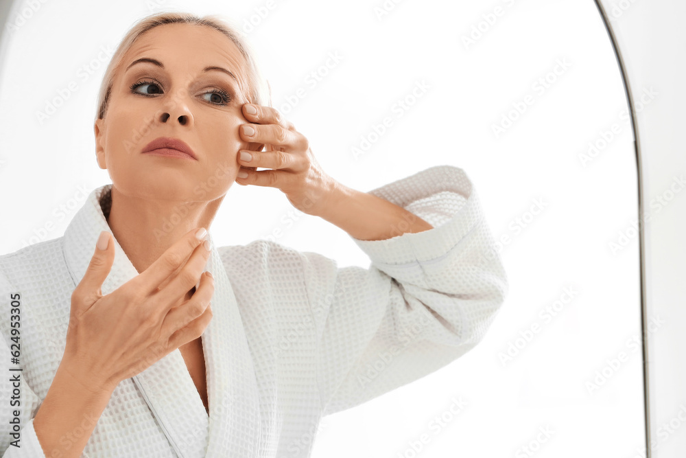 Mature woman doing face building exercise near mirror in bathroom