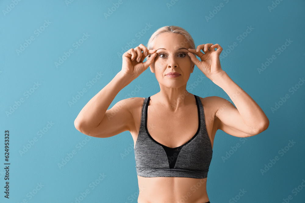 Sporty mature woman doing face building exercise on blue background