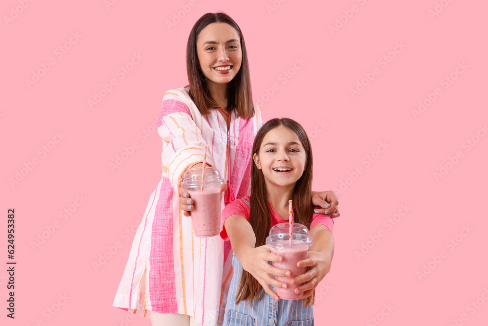 Little girl with her mother drinking smoothie on pink background