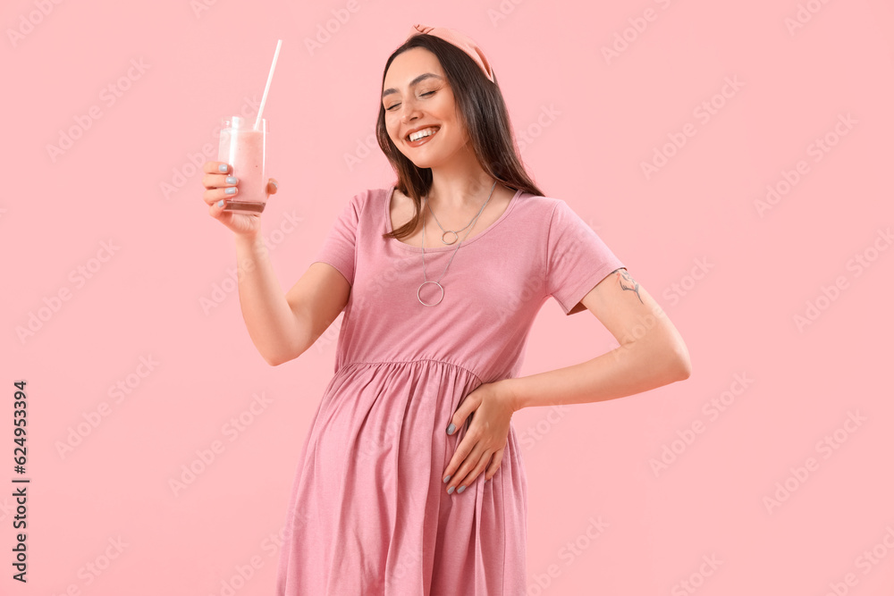 Young pregnant woman with glass of smoothie on pink background