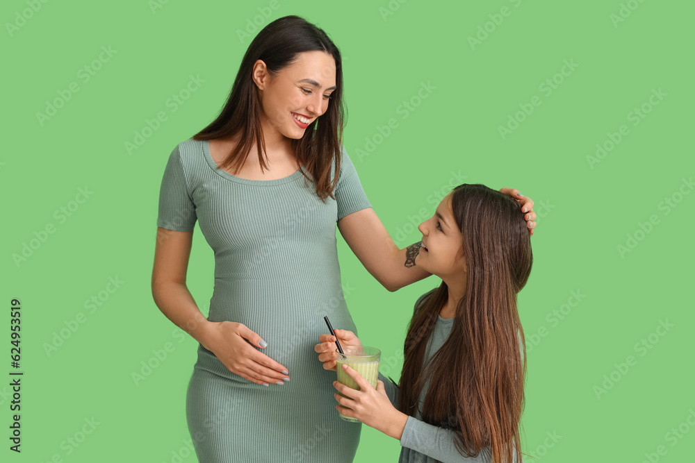 Little girl with glass of smoothie and her pregnant mother on green background