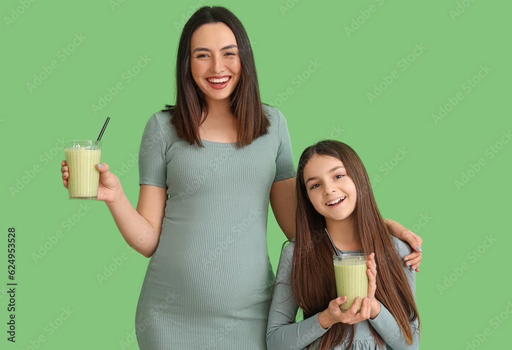 Little girl with her pregnant mother drinking smoothie on green background