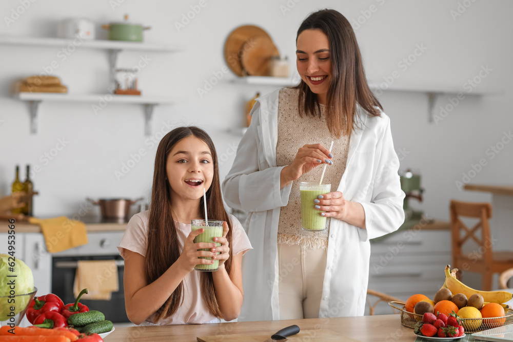 Little girl with her pregnant mother drinking green smoothie in kitchen