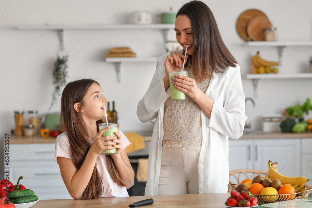 Little girl with her pregnant mother drinking green smoothie in kitchen