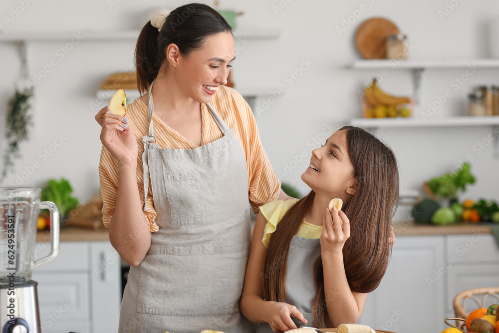 Little girl with her mother eating fruits while making smoothie in kitchen