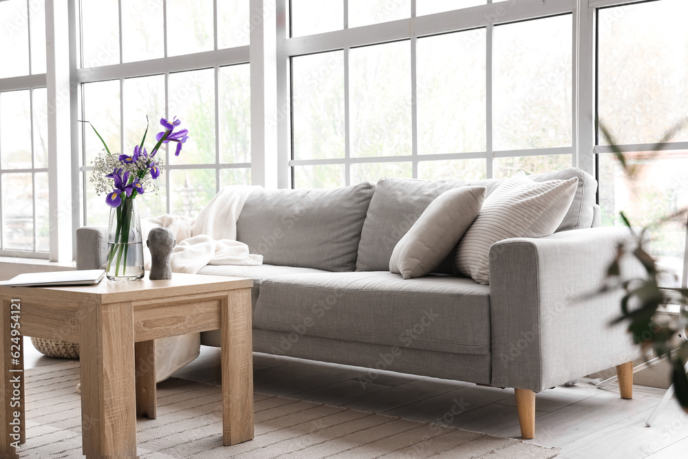 Interior of light living room with grey sofa and big window