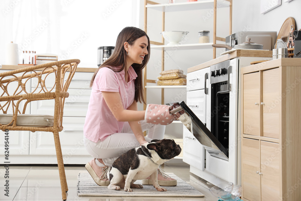 Young woman with her dog opening electric oven in kitchen