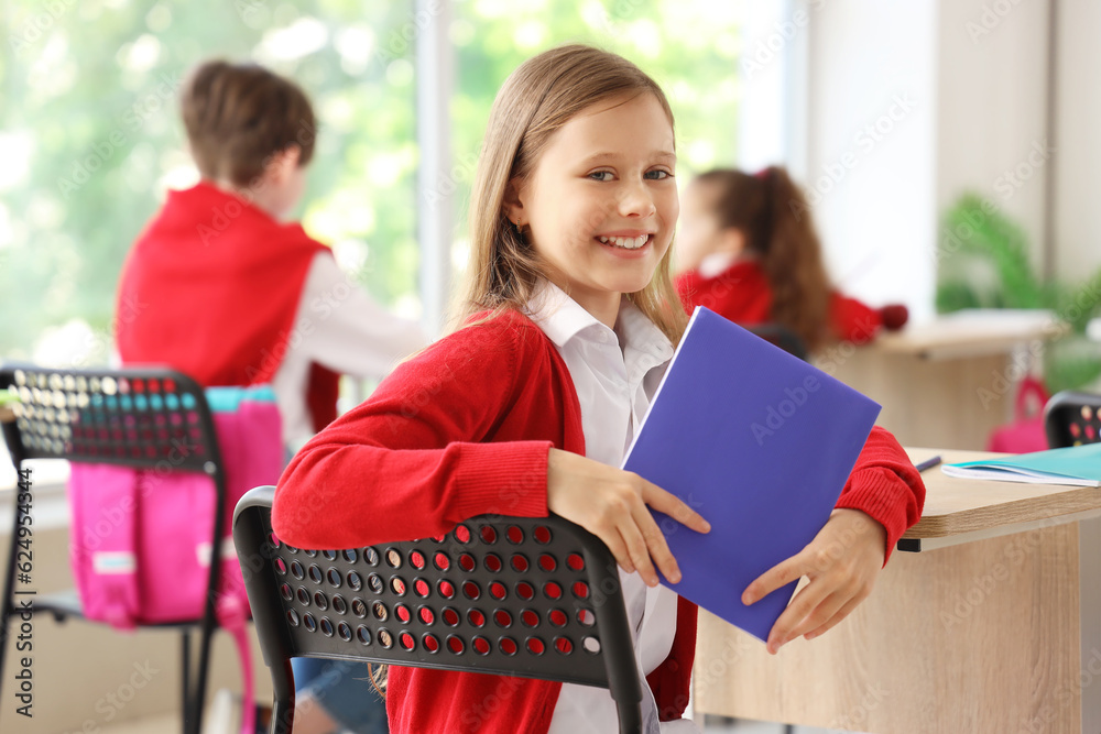 Little schoolgirl with copybook in classroom