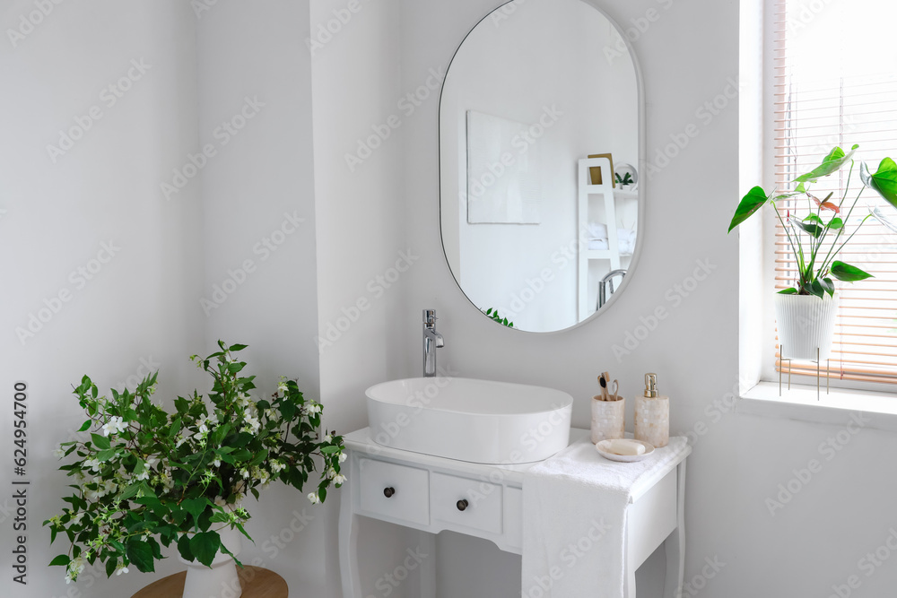 Sink bowl and bath accessories on dressing table in interior of light bathroom