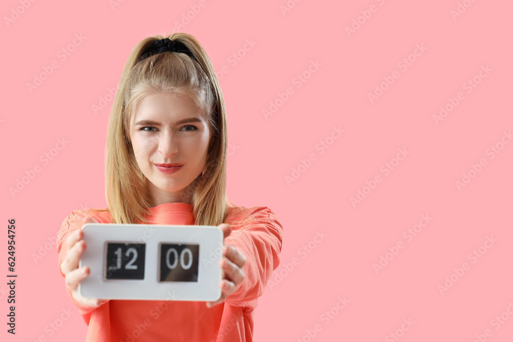 Stressed young woman with clock on pink background. Deadline concept